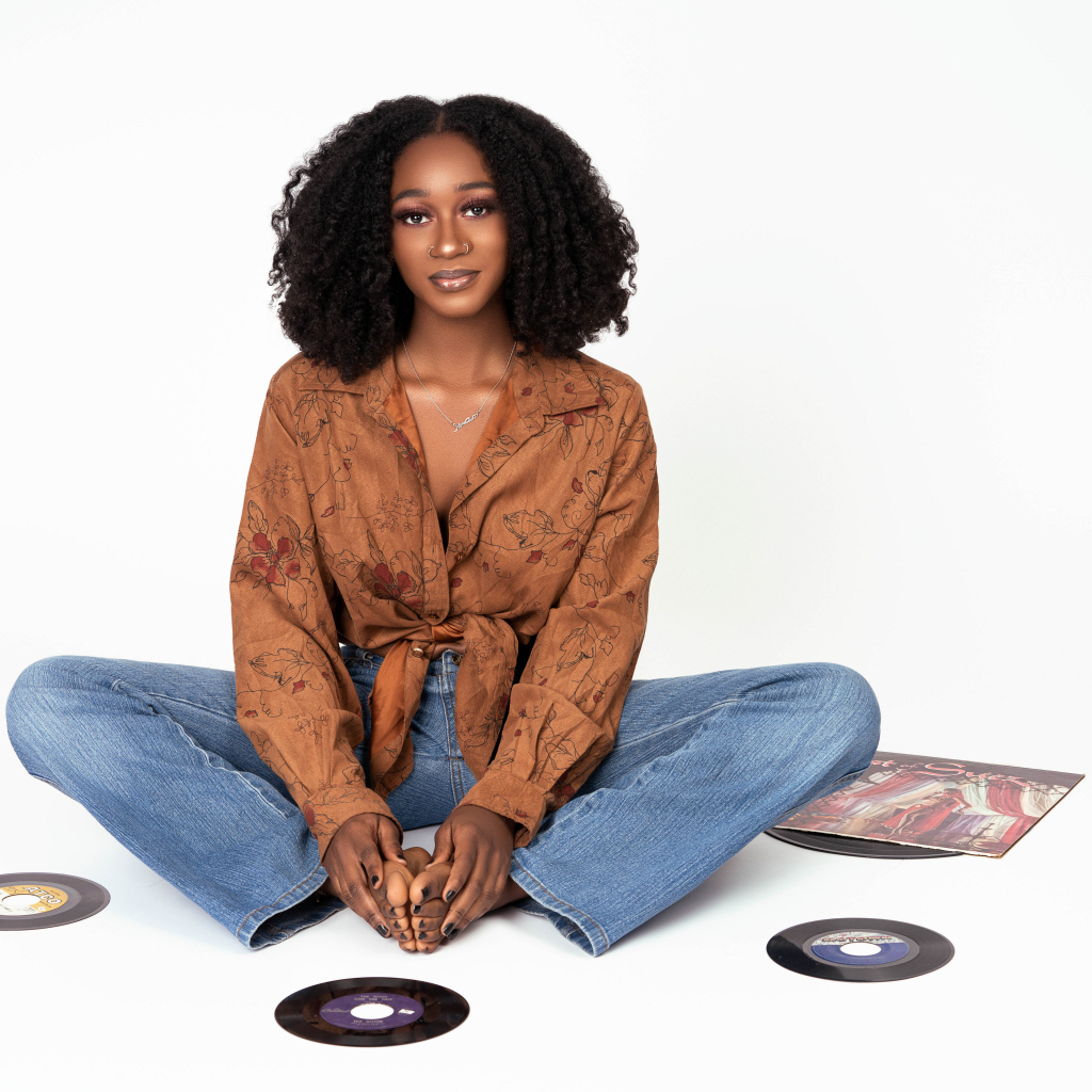 Темнокожая девушка сидит на белом фоне с пластинками