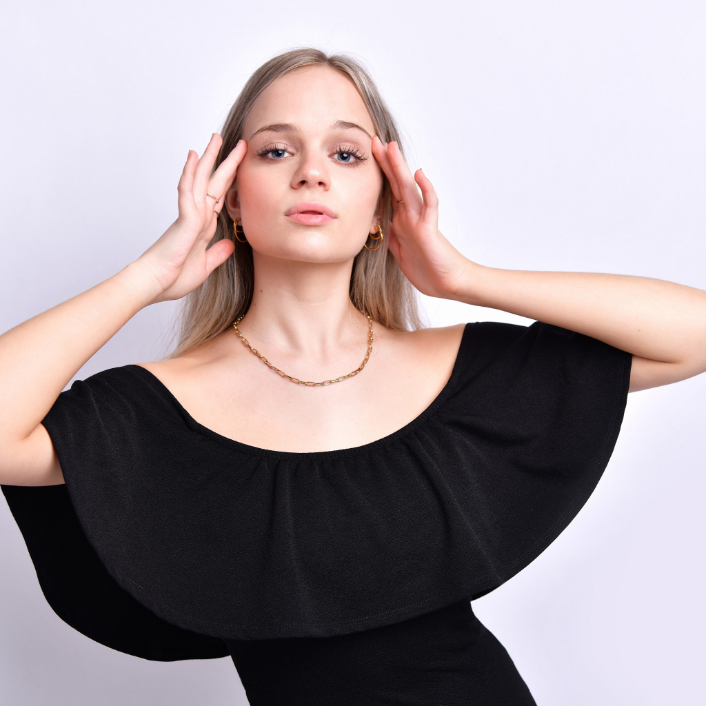 Девушка в черном платье с руками у головы на белом фоне