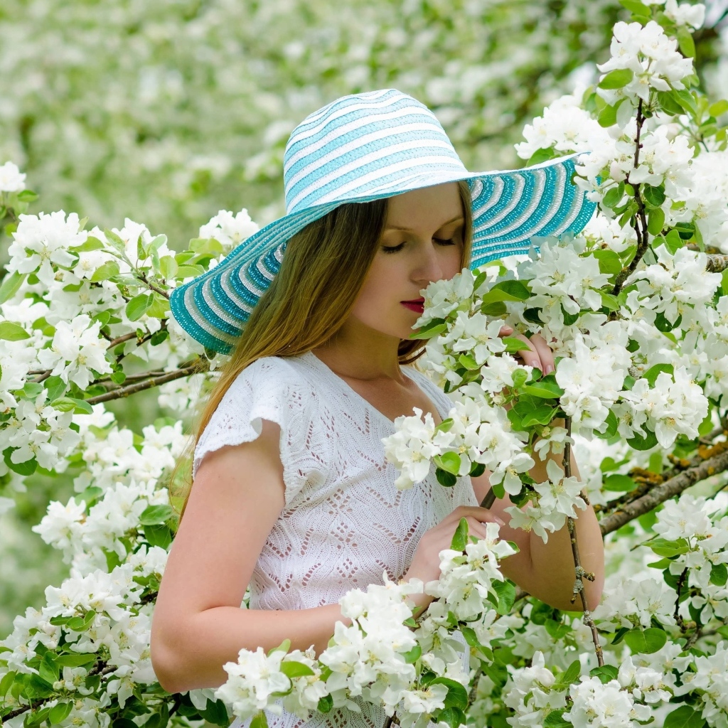 Девушка в шляпе нюхает ветку яблони 