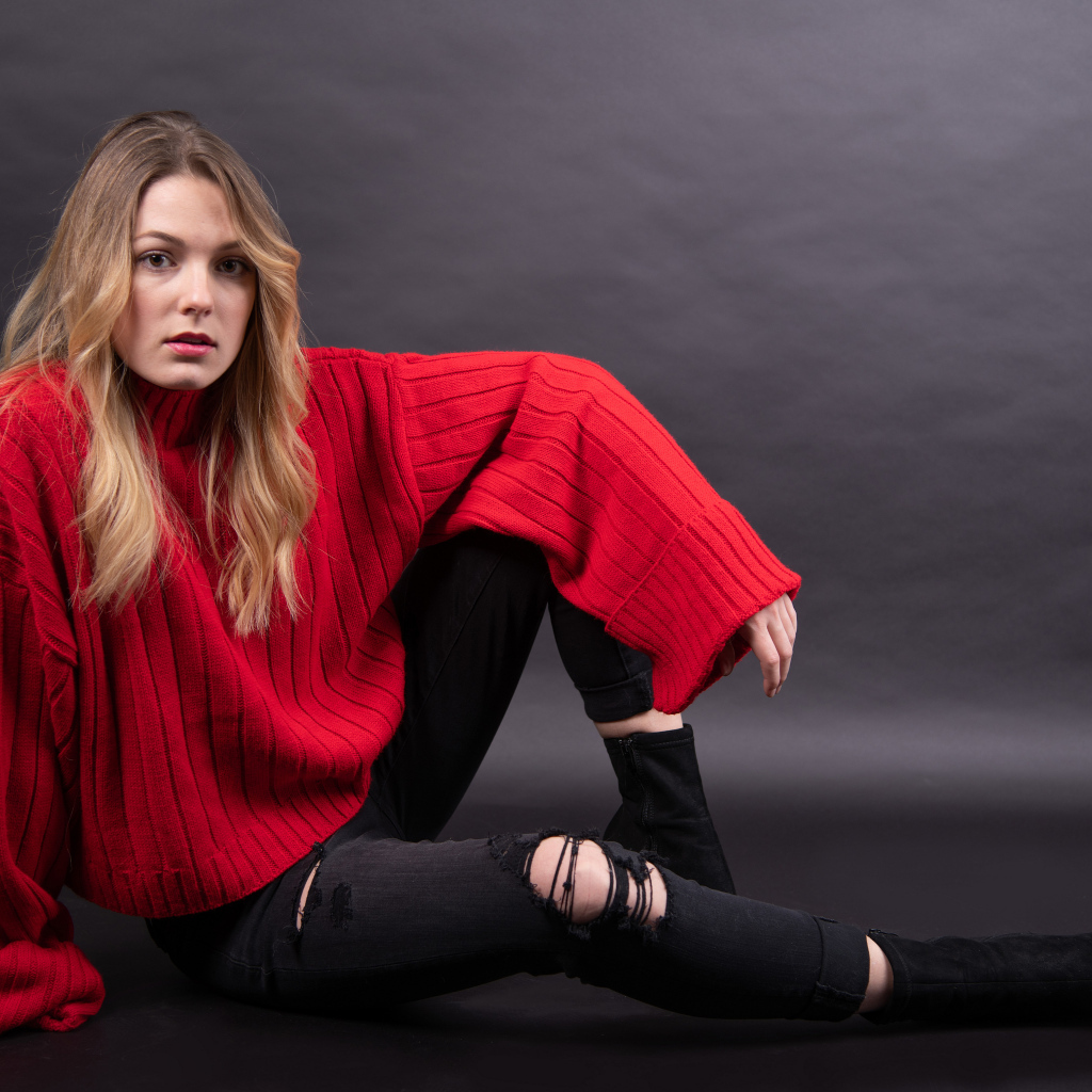 Девушка в красном свитере сидит на сером фоне