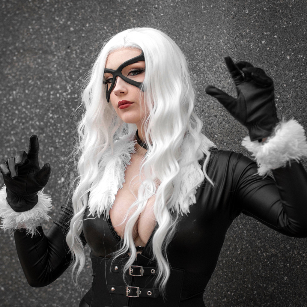 Девушка в белом парике в черном костюме у серой стены