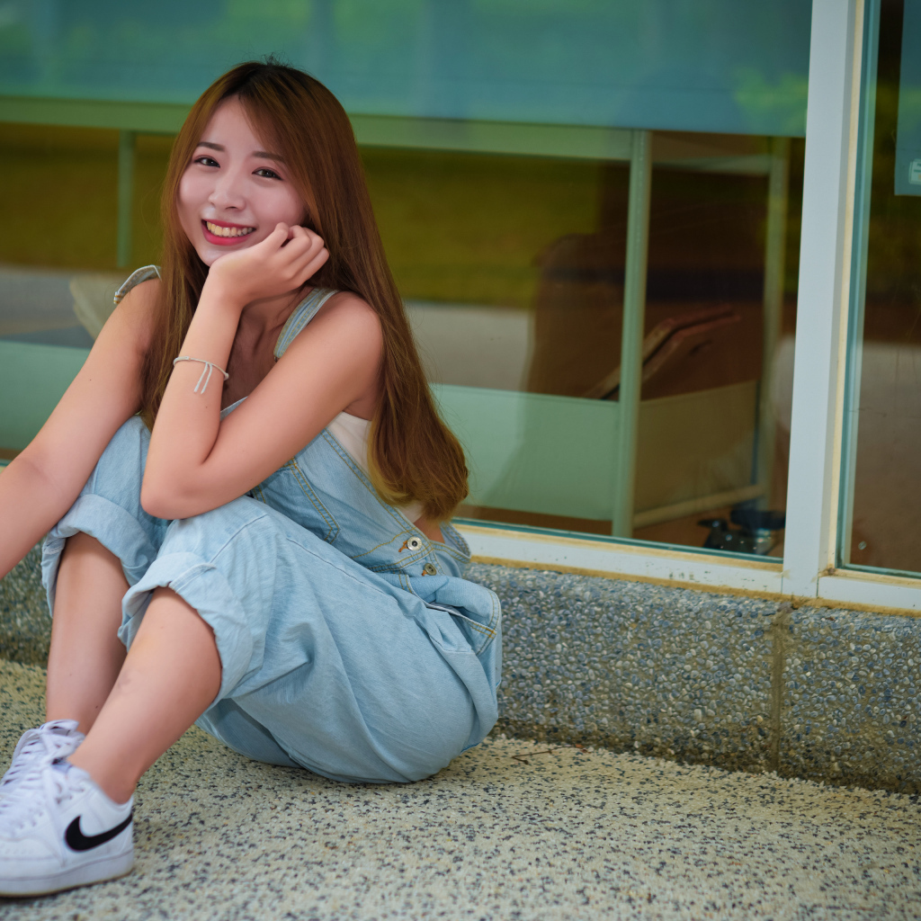 Девушка в джинсовом комбинезоне сидит на полу