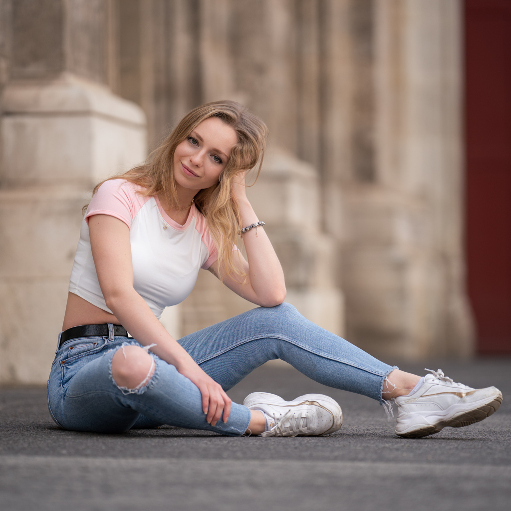 Девушка в рваных джинсах сидит на асфальте