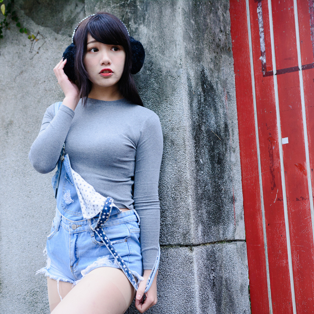 Скромная девушка азиатка в наушниках стоит у стены