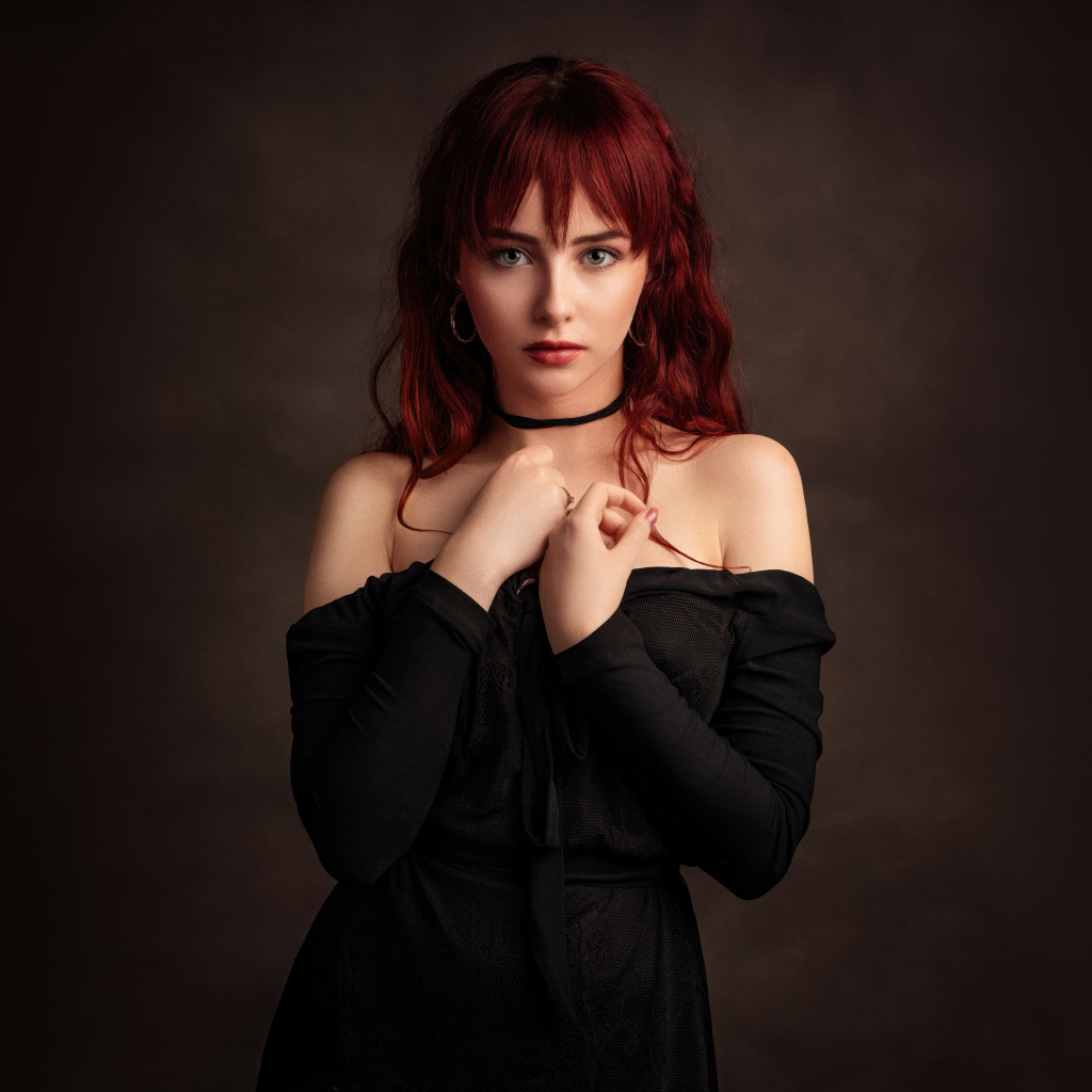 Рыжеволосая девушка в черном платье у стены