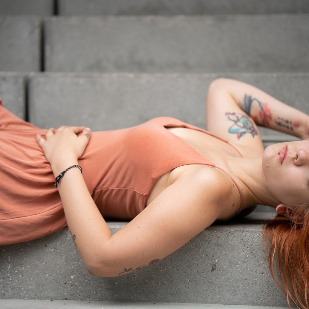 Рыжеволосая девушка с татуировками лижет на ступеньках