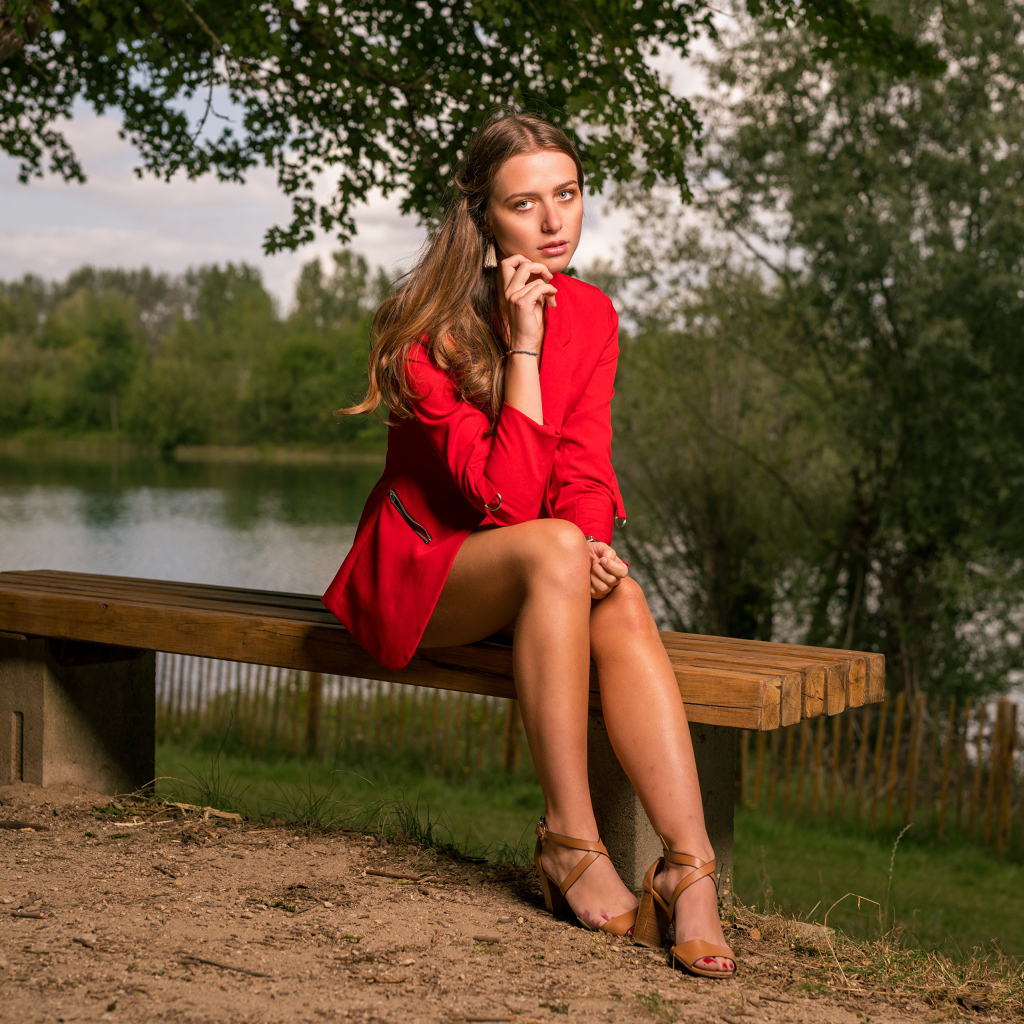 Грустная девушка в красном пальто сидит на лавке