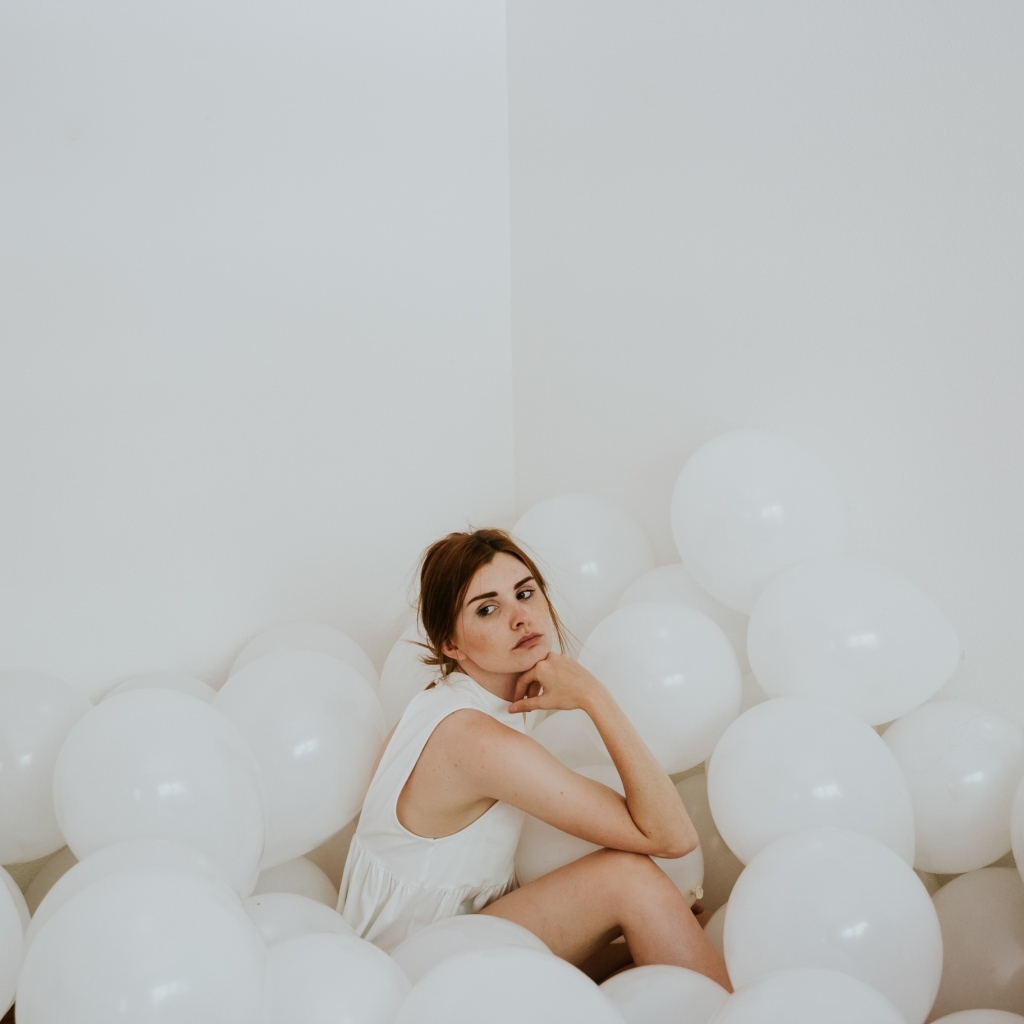 Грустная девушка сидит в белых воздушных шариках