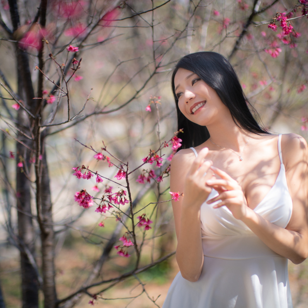 Улыбающаяся девушка в белом платье у дерева с цветами