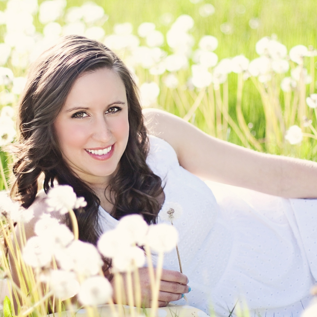 Улыбающаяся девушка лежит на поле с одуванчиками