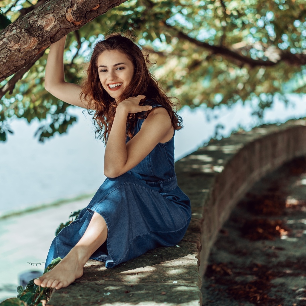 Улыбающаяся девушки сидит у дерева