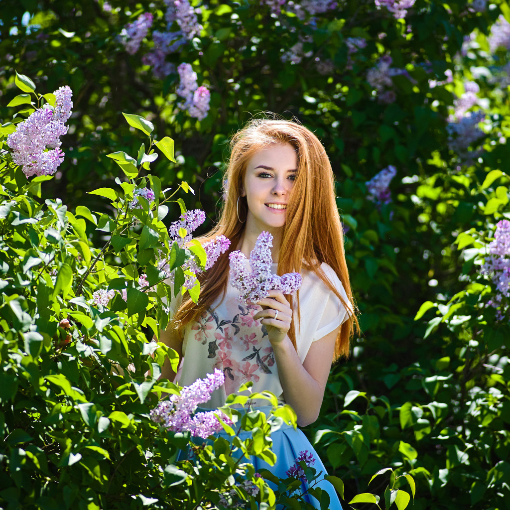 Улыбающаяся девушка стоит у куста сирени