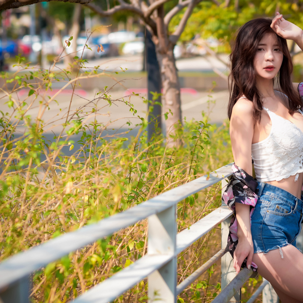 Молодая азиатка в синих шортах стоит у забора