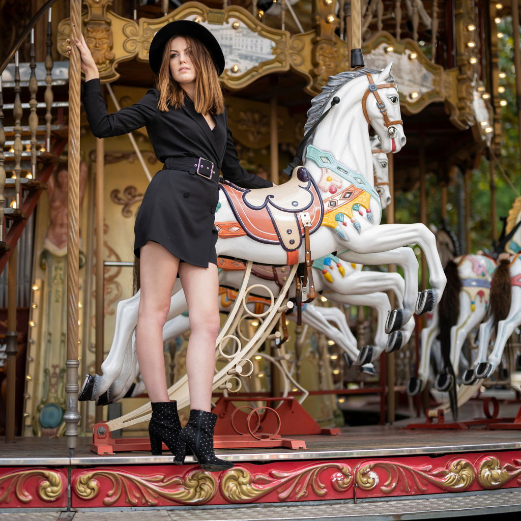 Молодая девушка в черном платье у карусели в парке