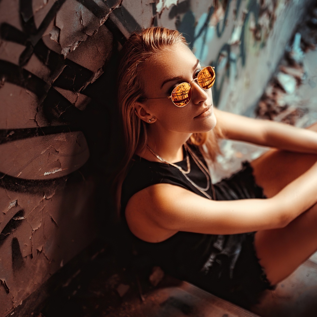 Молодая девушка в очках сидит у стены