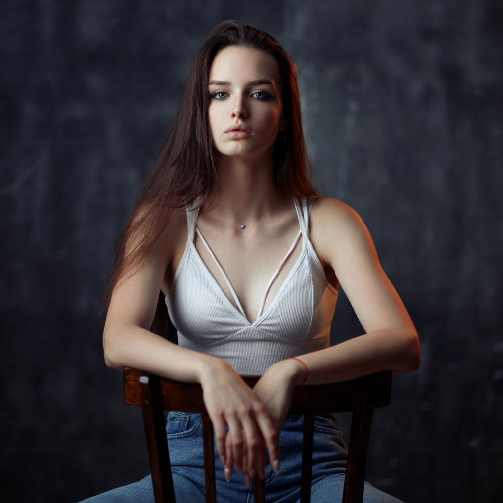 Молодая длинноволосая девушка сидит на деревянном стуле