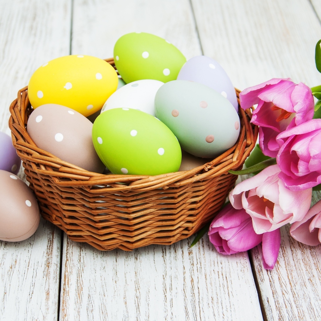 Корзина разноцветных яиц с тюльпанами на столе на Пасху