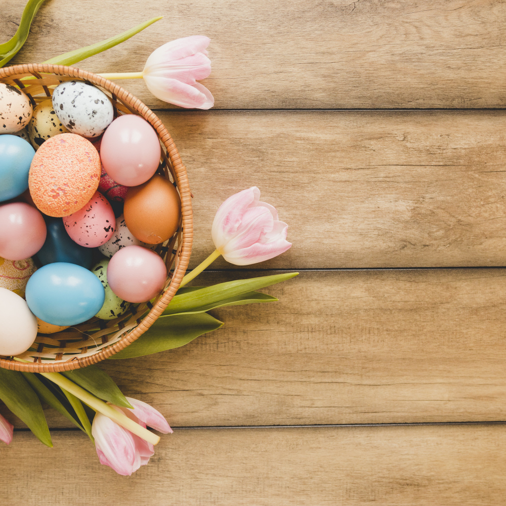 Корзина с крашеными яйцами и розовые тюльпаны на деревянном столе на Пасху