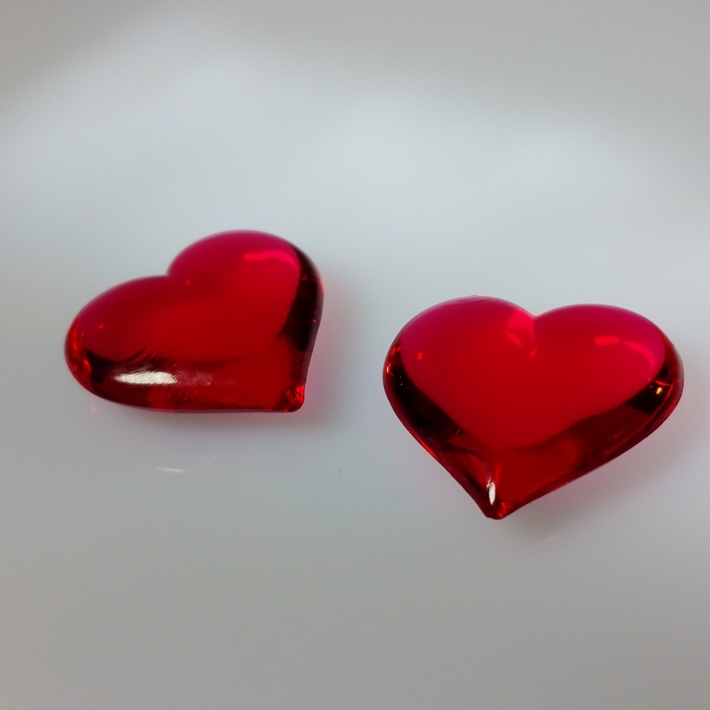Два красных стеклянных сердца на сером фоне
