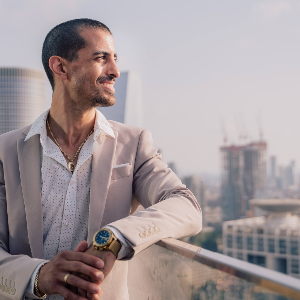 Улыбающийся стильный мужчина в костюме стоит на балконе 