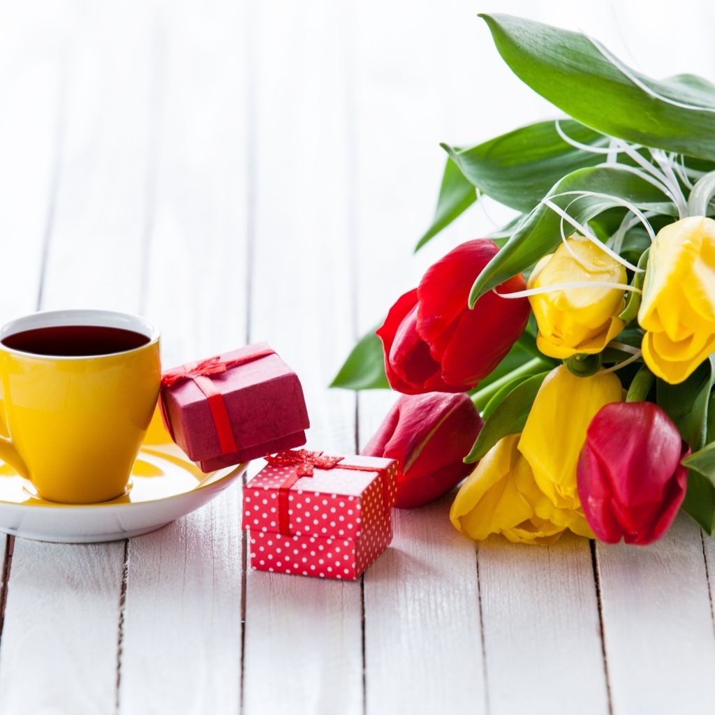 Желтая чашка кофе на столе с подарками и букетом тюльпанов