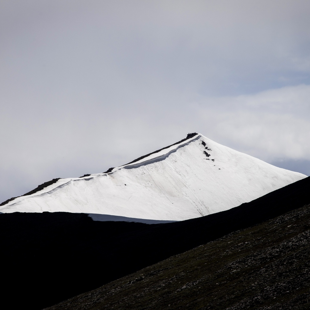 Заснеженная вершина горы под грозовым небом