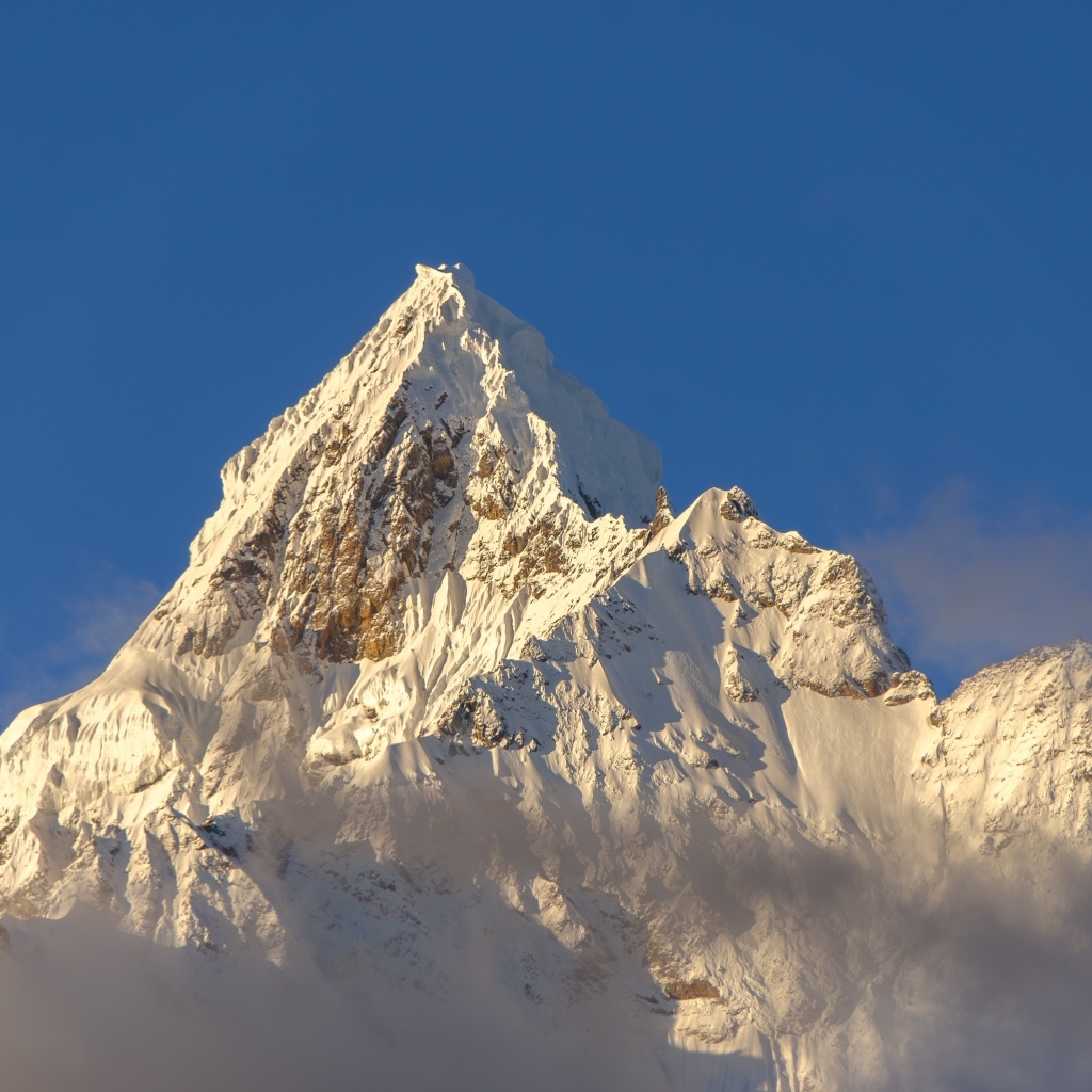 Крутая заснеженная вершина горы на голубом фоне