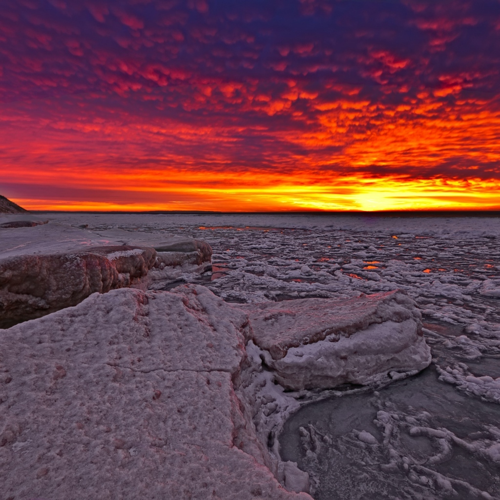 Красный закат солнца покрывает заледеневшее озеро 