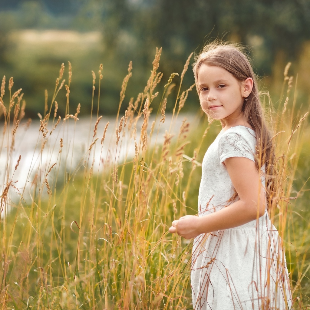 Маленькая девочка в белом платье гуляет по высокой траве