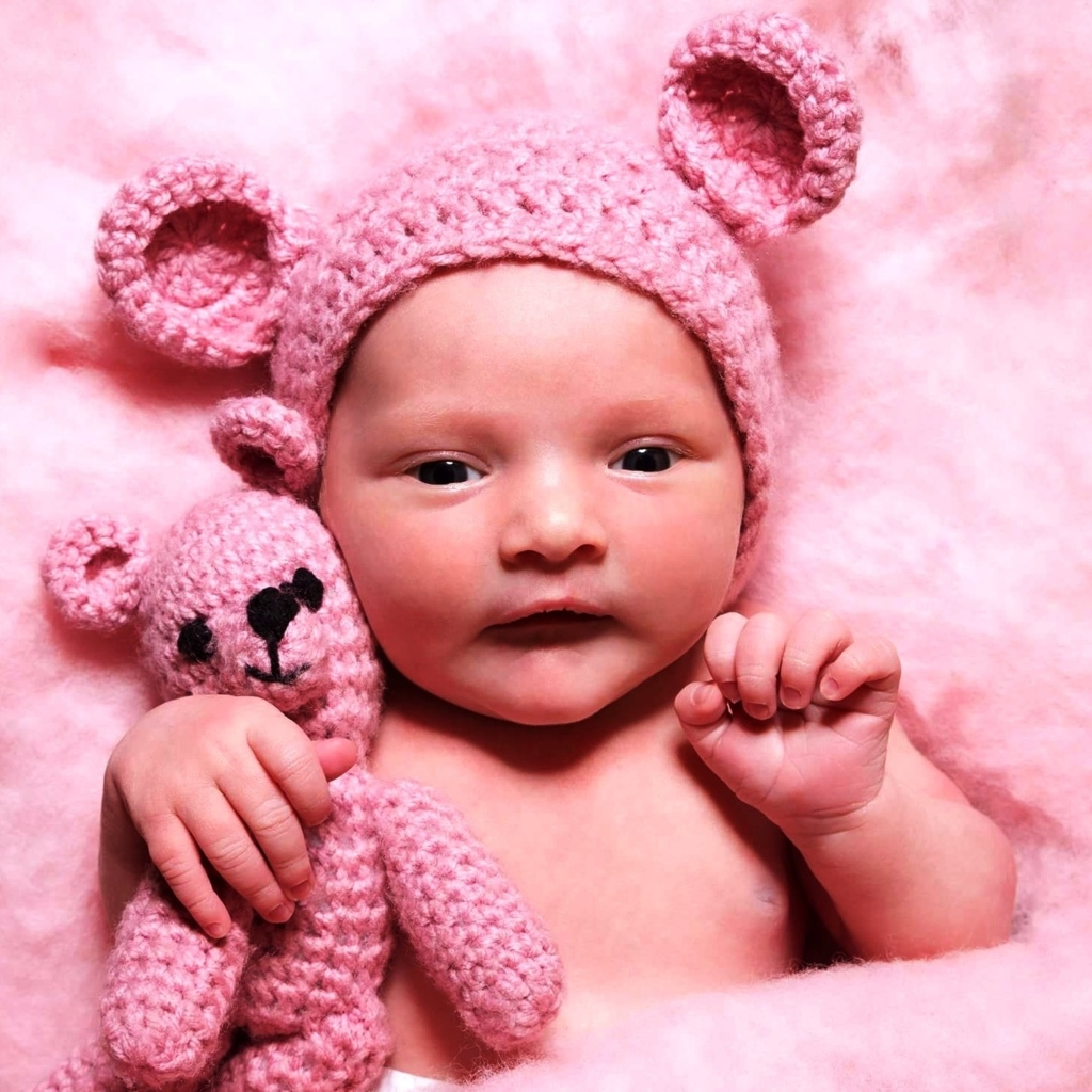 Грудной ребенок в розовой шапке с игрушкой в руке