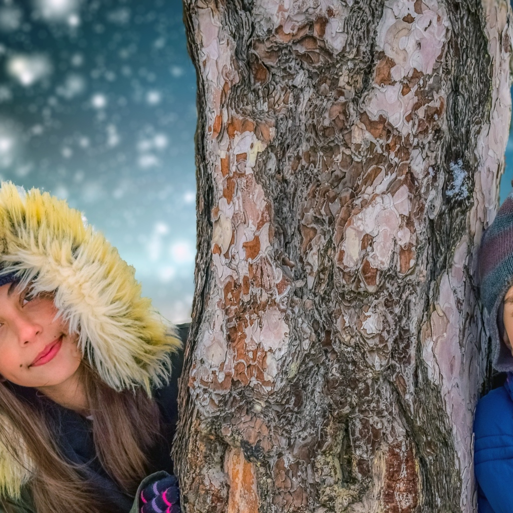 Мальчик и девочка стоят у дерева зимой