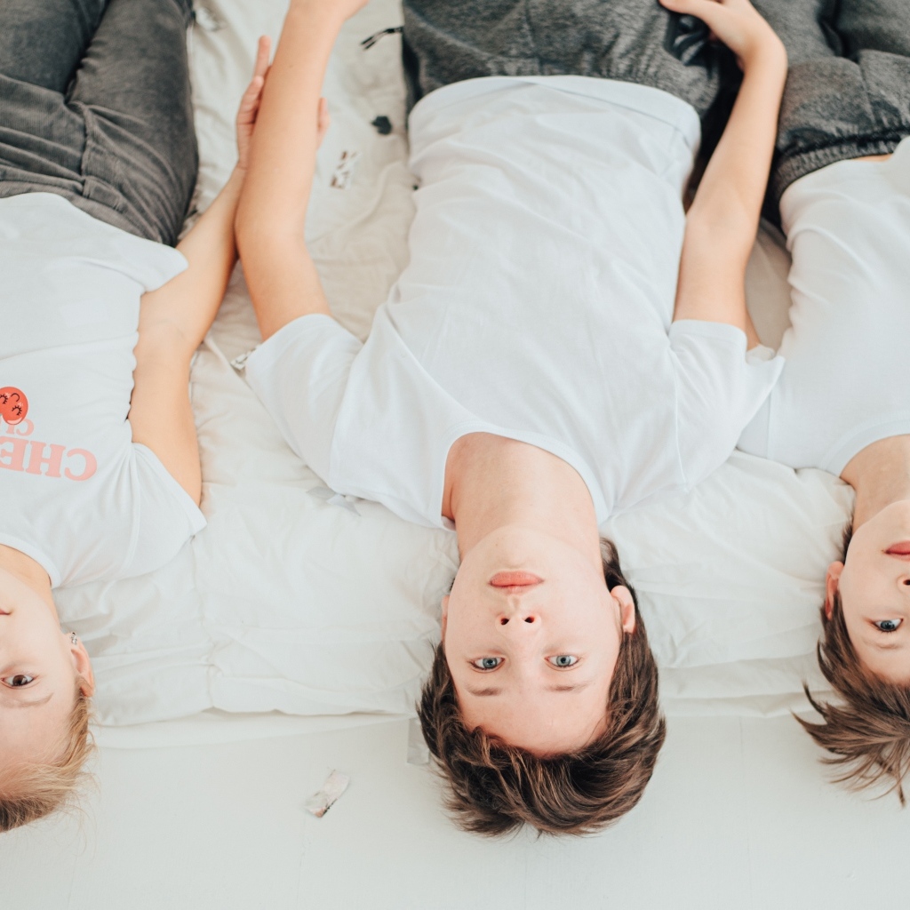 Дети в белых футболках лежат на кровати