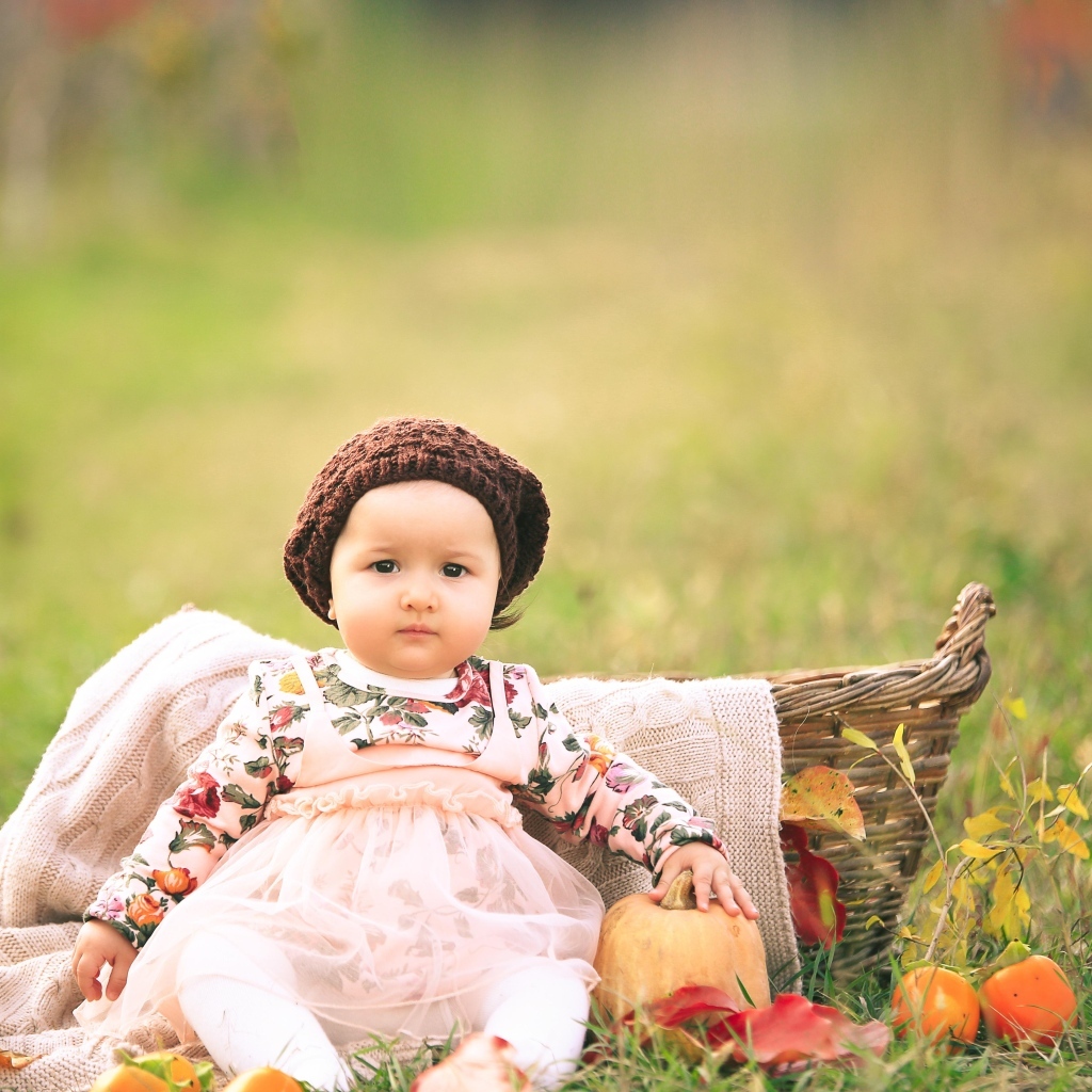 Милая маленькая девочка в шапке сидит на траве 