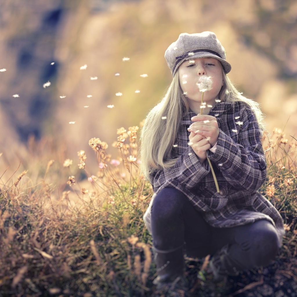 Девочка в кепке сдувает одуванчик