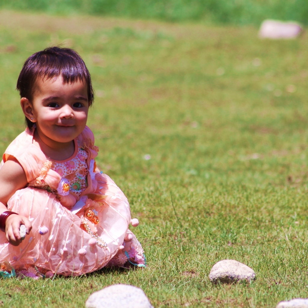 Девочка в розовом платье играет на зеленой траве