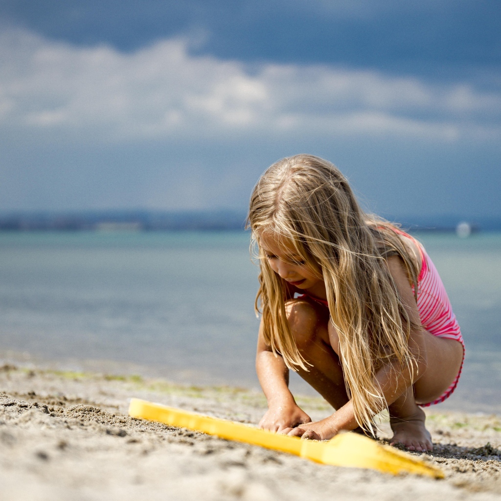 Девочка играет на песке у моря