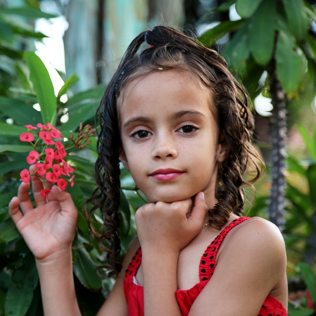 Девочка стоит у ветки с красными цветами