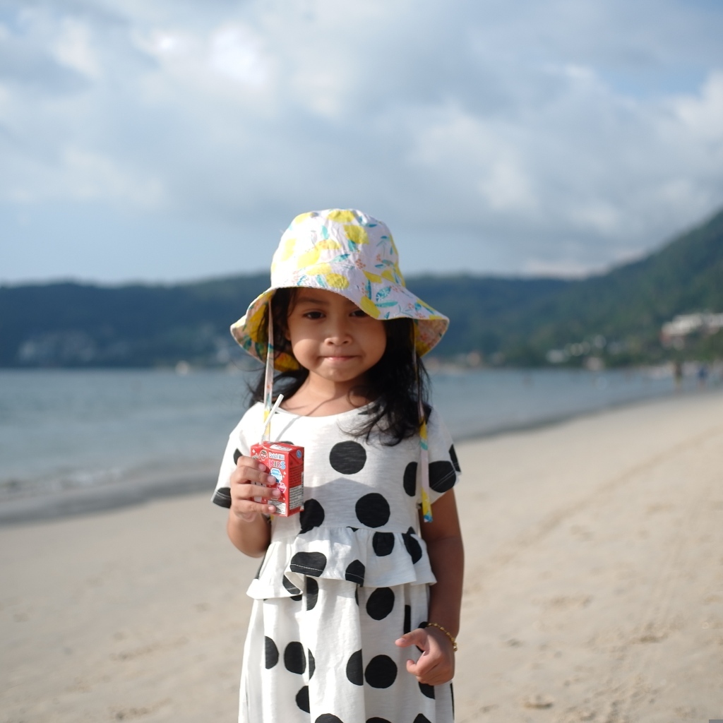 Девочка с соком в руках стоит на пляже