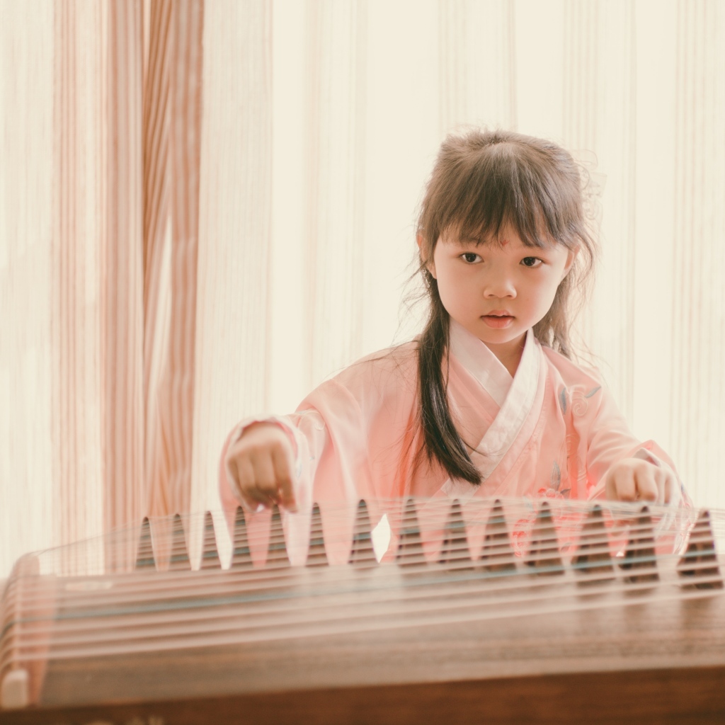 Маленькая девочка азиатка играет на музыкальном инструменте