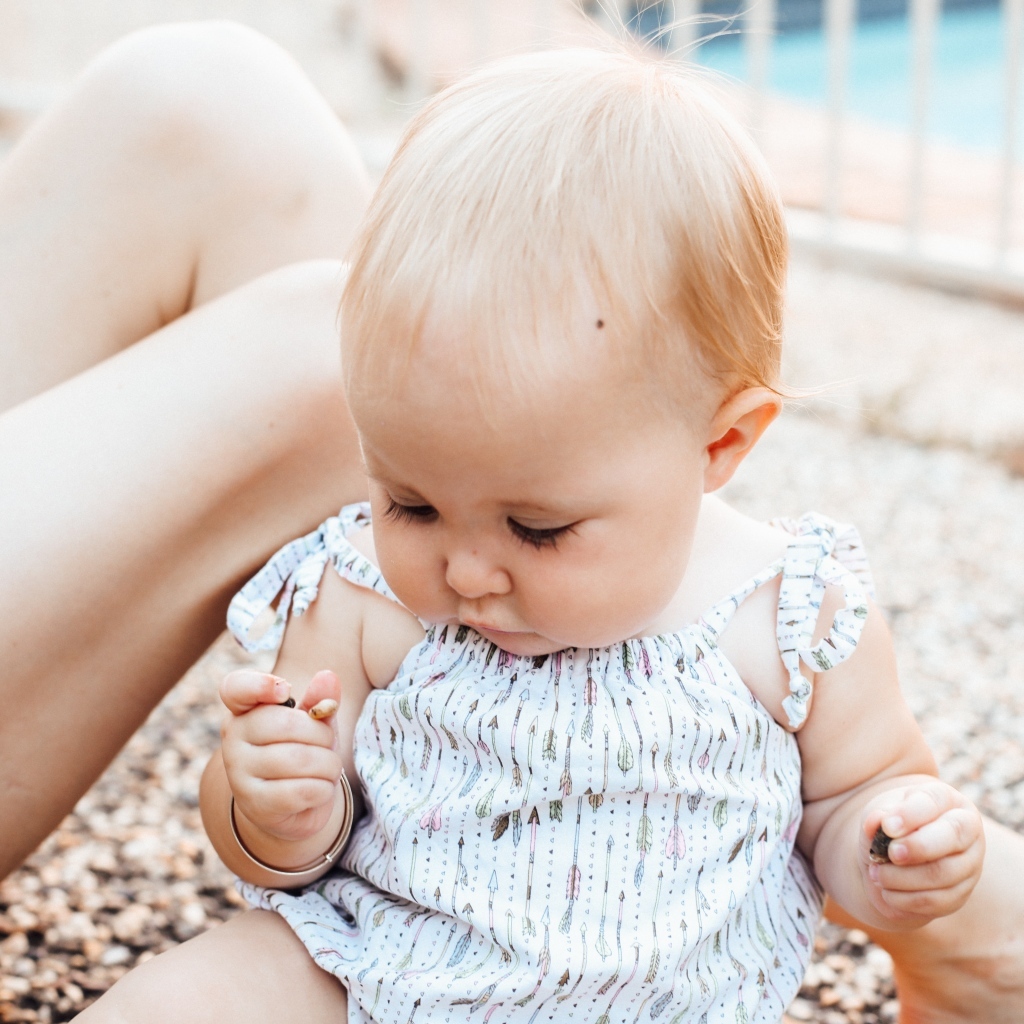 Маленькая светловолосая девочка сидит на песке