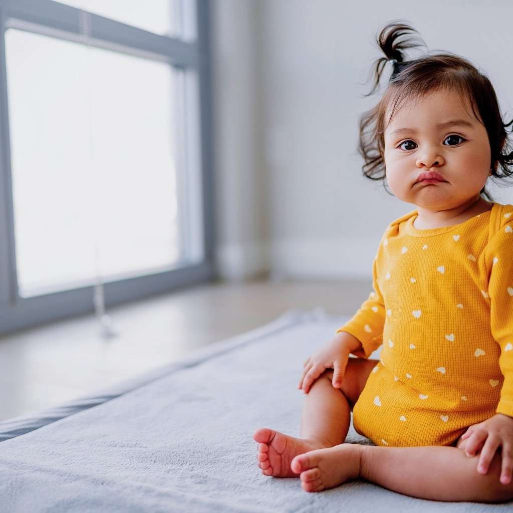 Маленькая смешная девочка сидит у окна