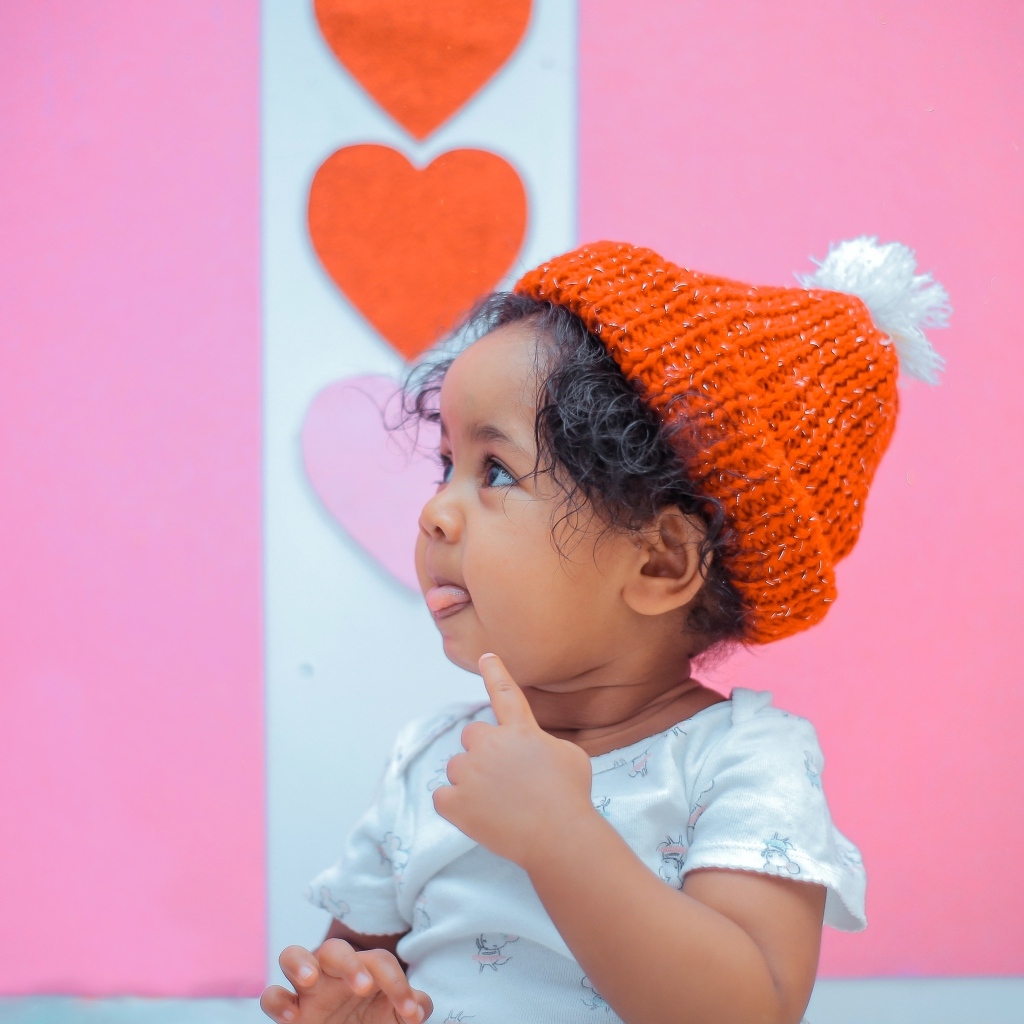 Маленькая девочка в вязаной шапке на розовом фоне