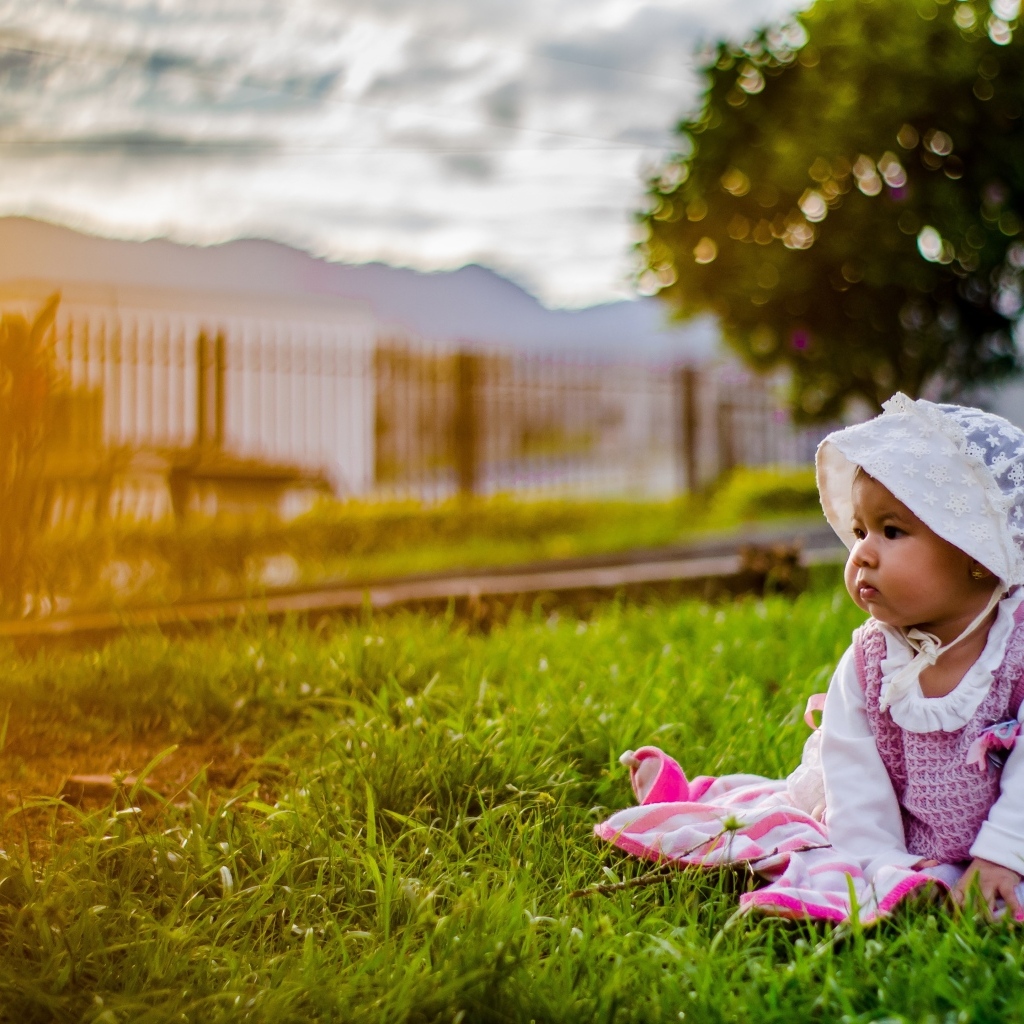Маленькая девочка в розовом платье сидит на траве