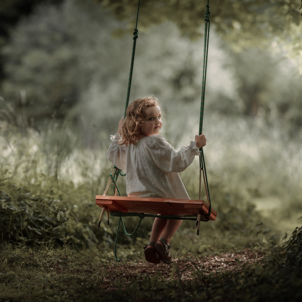Маленькая девочка на качели в саду