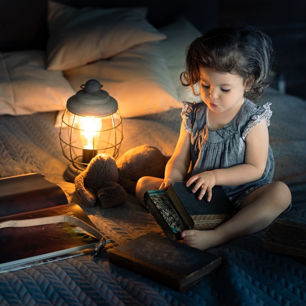 Маленькая девочка читает книги на кровати