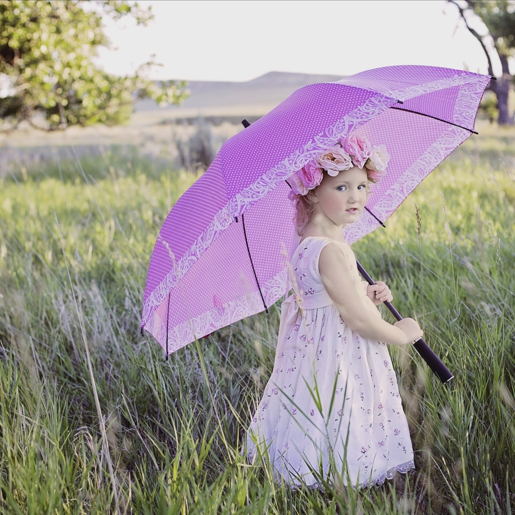 Маленькая девочка стоит в траве с зонтом