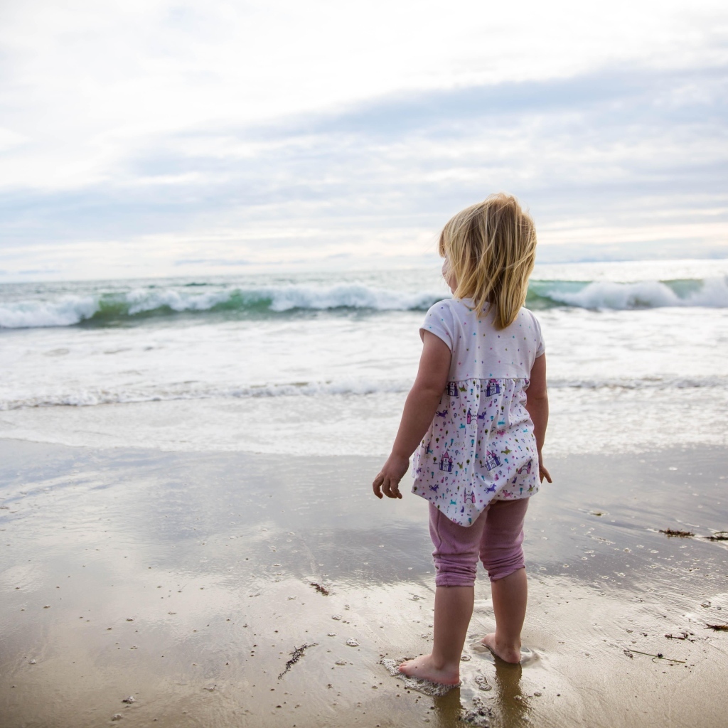 Маленькая девочка стоит на берегу моря
