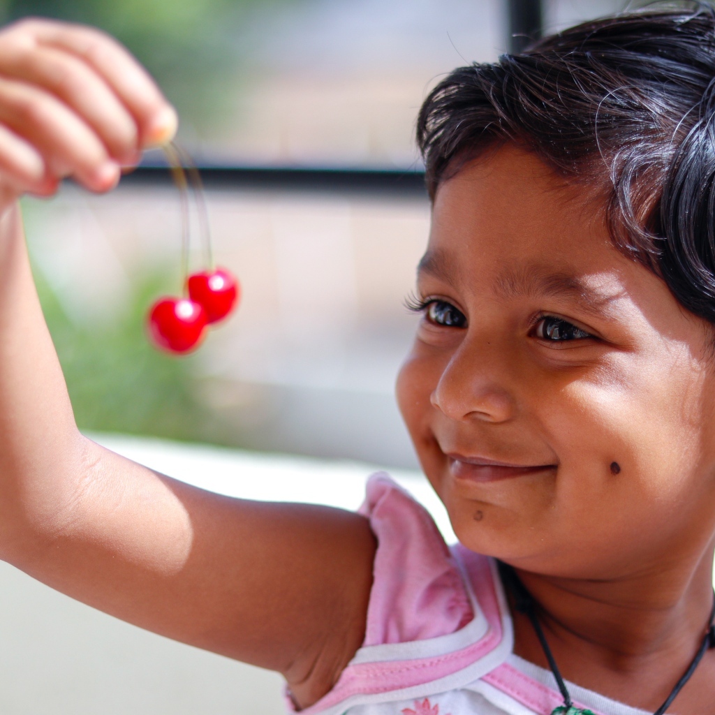 Маленькая улыбающаяся девочка с ягодами вишни в руках