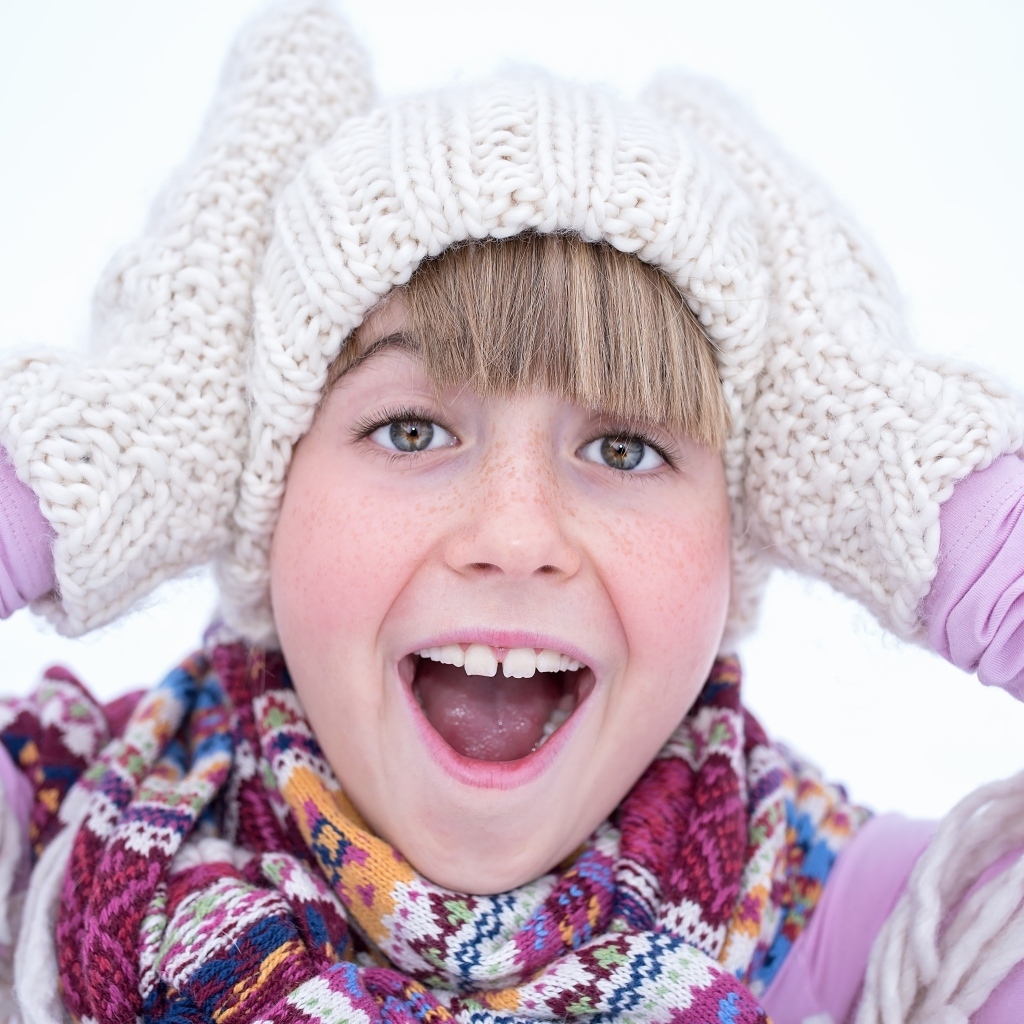 Довольная девочка в вязаной шапке и варежках