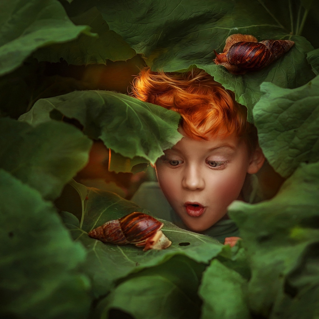 Удивленный рыжеволосый мальчик смотрит на улитку